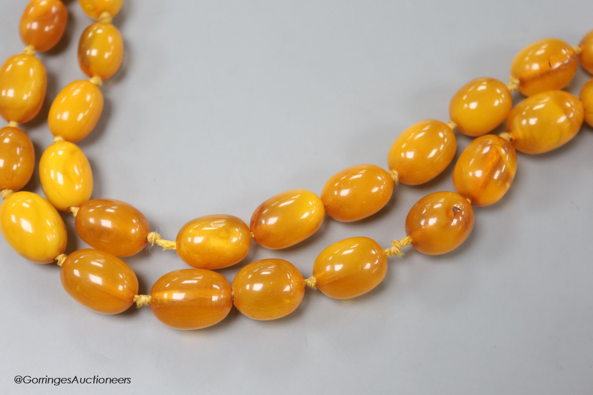 Two single strand graduated oval amber bead necklaces, 71cm, 61 grams & 89cm, 68 grams (beads missing from larger necklace)